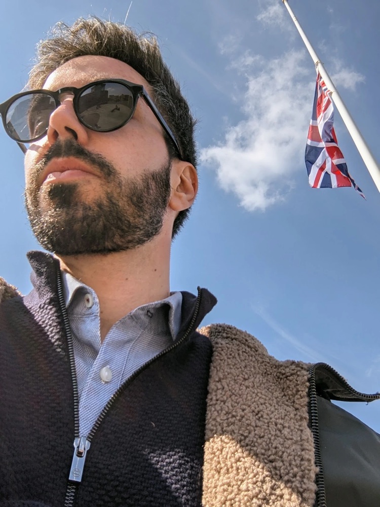 André in sunglasses on a sunny day, a Union Jack flying behind him